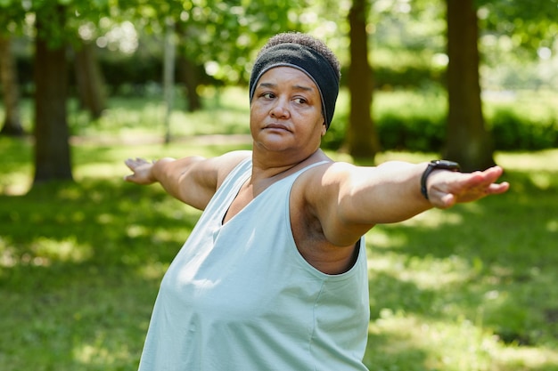 Waist up portrait of overweight black woman working out outdoors in park and stretching arms out