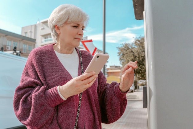 Waist-up portrait of a senior woman using the payment terminal at the self-service gas station