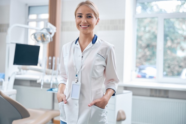 Waist up portrait of smiling young woman standing in modern office with digital equipment during working day