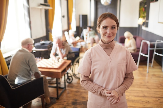 Waist up portrait of smiling young woman wearing uniform in nursing home copy space