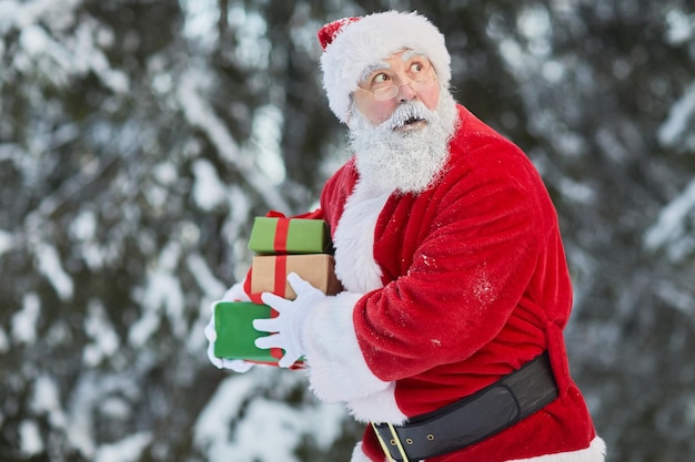 Waist up portrait of traditional santa claus carrying presents in secret outdoors and looking cautio