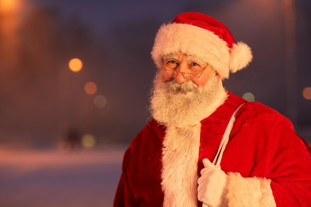 Waist up portrait of traditional santa claus standing in city street at night and smiling at camera