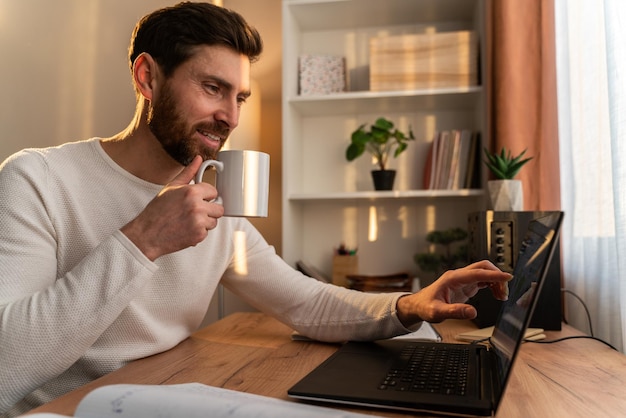 Waist up portrait view of the good-looking young man working on notebook at home while drinking his coffee. Stock photo