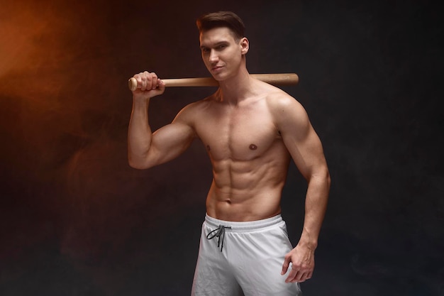 Waist up portrait view of muscle man posing in studio with baseball bat