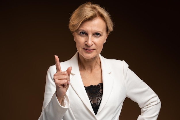 Waist up portrait view of serious strict mature business woman gesturing with her finger while posing isolated over black wall background. Stock photo