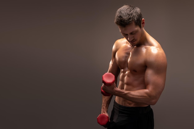 Waist up portrait view of the well shaped young man with dumbbells in hands on brown background. Sport and recreation concept