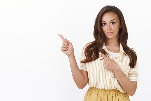 Waist-up shot gorgeous sassy brunette pointing fingers upper left corner and smiling, telling best choice to buy, showing perfect offer, giving advice where find best deals