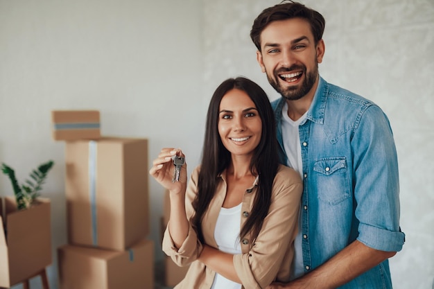 Waistup photo of an excited young man and his beautiful wife looking happy and showing keys from a new appartment