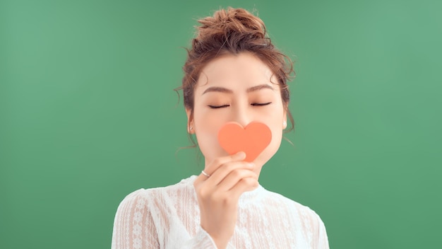 Waistup portrait of pretty Asian woman looking away with toothy smile while holding Valentines Day card in hands white background