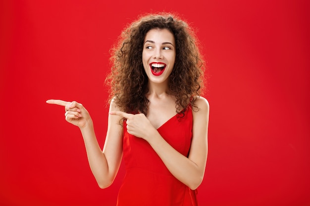 Waistup shot of amused and entertained charming happy female with curly hairstyle in elegant evening...