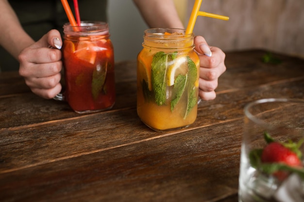 Waiter brings jars of fresh fruit cocktails to customer Orange and strawberry cold drink with mint and ice on wooden table refreshment and satisfying thirst in hot weather free space