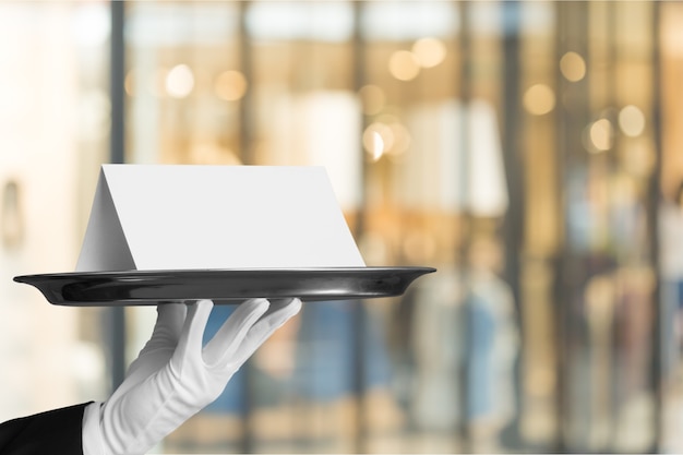 Waiter or butler wearing a tuxedo holding a note card on a silver tray in front of his torso.