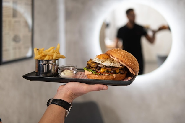 Waiter Holding the Plate With Hamburger and Fries in the Restaurant