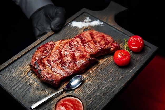 The waiter holds a dish with steak with sauce and tomatoes