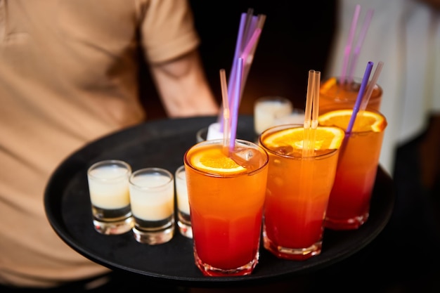 The waiter holds a tray with Multicolored alcoholic and nonalcoholic cocktails with ice and straws