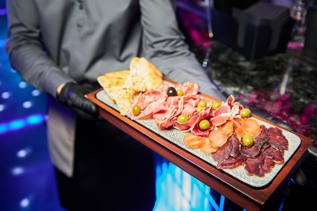 The waiter holds a wooden plate with various sliced dried delicacies