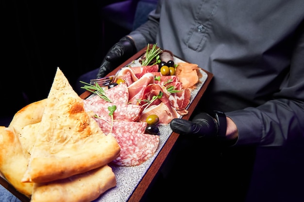 The waiter holds a wooden plate with various sliced dried delicacies