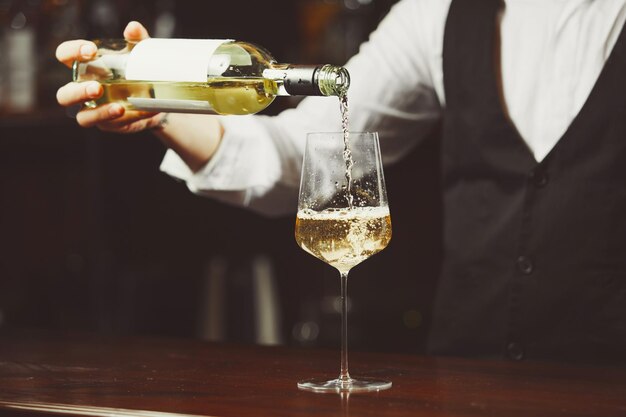 Waiter pours white wine into a glass closeup