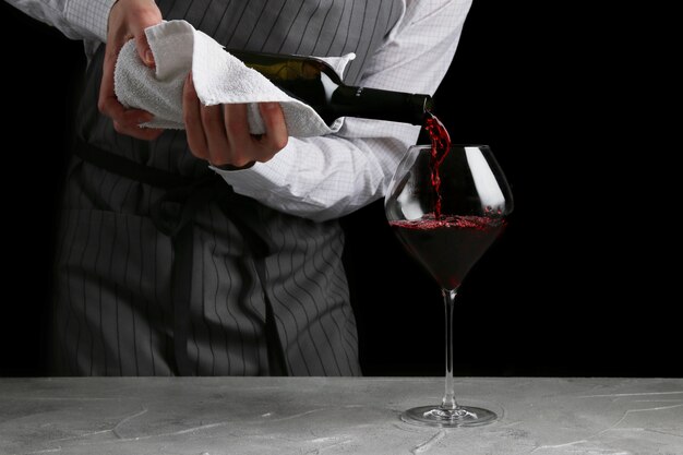 The waiter pours wine in glass on dark background