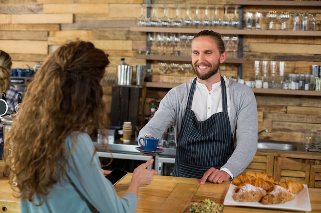 Waiter serving a cup of coffee to customer at counter