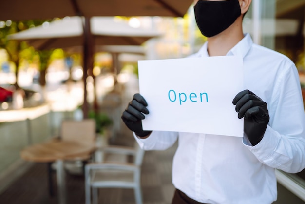 Waiter wearing protective face mask and gloves while disinfecting tables at outdoor cafe