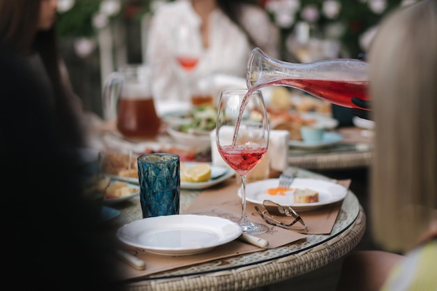 Waiteress pouring rose wine in glass background of people eating dinner at summer terrace in cafe