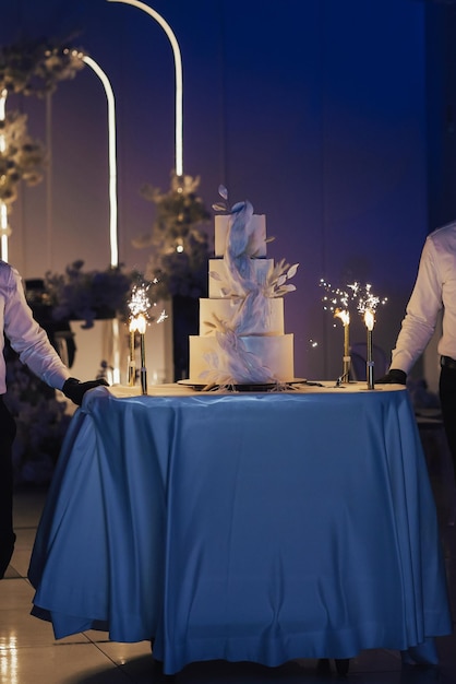 Waiters bear four tier wedding cake with a fountains on the cake