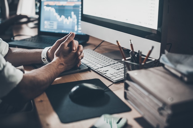 Waiting for new ideas. Close-up of young businessman keeping hands together while sitting at the desk in creative office