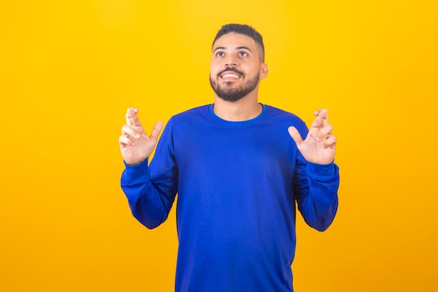 Waiting for a special moment Portrait of young man in shirt keeping fingers crossed on yellow background