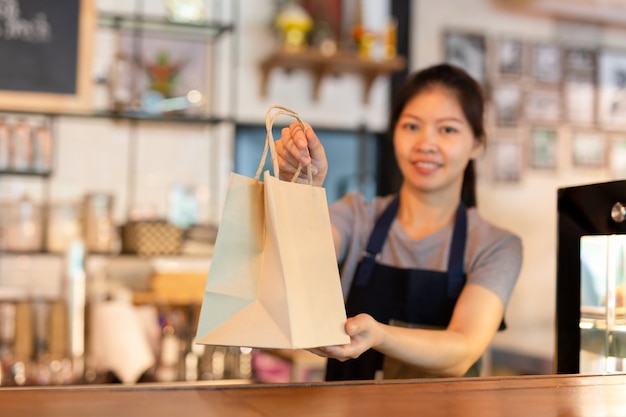 Waitress at counter giving eco friendly paper bag with take away drink in cafe