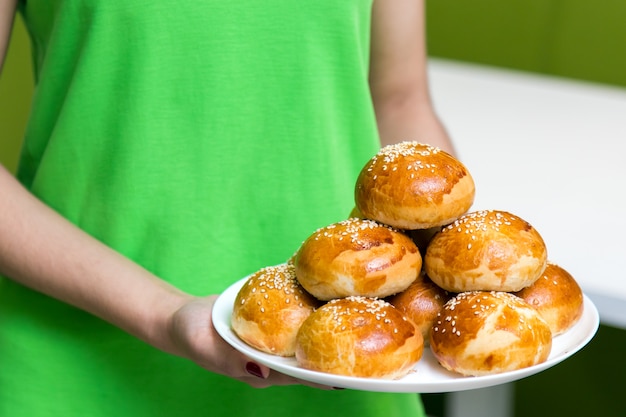 Waitress in a green uniform holding a plate with fresh tasty buns with sesame in cafe