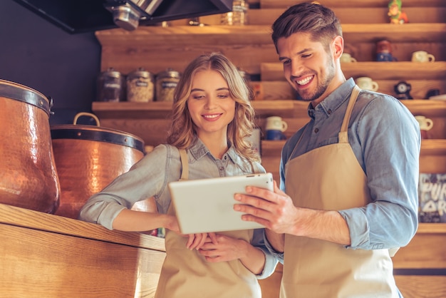 Waitress and young waiter in aprons are using a tablet.