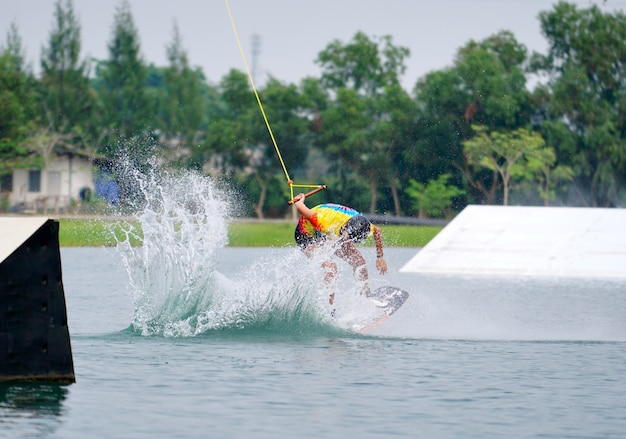 Wake boarding rider jumping trick with water splash in wake park.