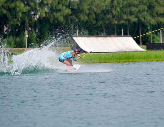 Wake boarding rider jumping trick with water splash in wake park.