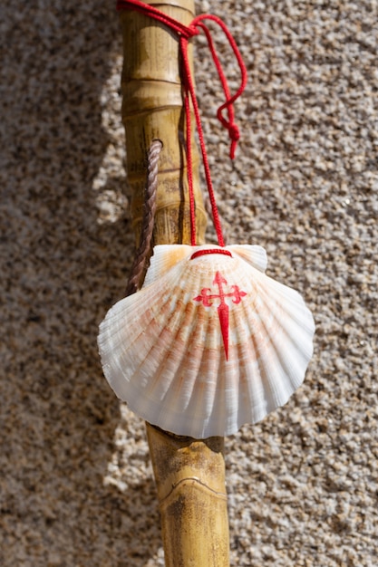 Walking stick and seashell of the Camino de Santiago leaning on granite stone wall. Santiago de Compostela pilgrimage concept