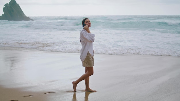 Walking woman talking smartphone looking at cloudy seascape girl speaking phone