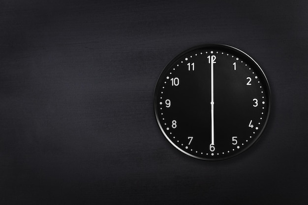 Wall clock showing six o'clock on black chalkboard background Office clock showing 6am or 6pm on black texture