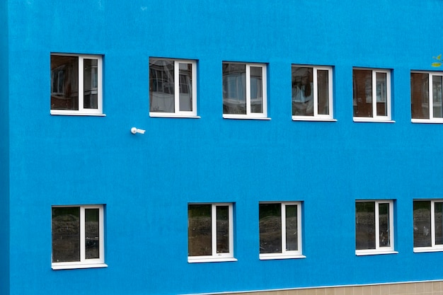 The wall of a new blue house with windows and a surveillance camera