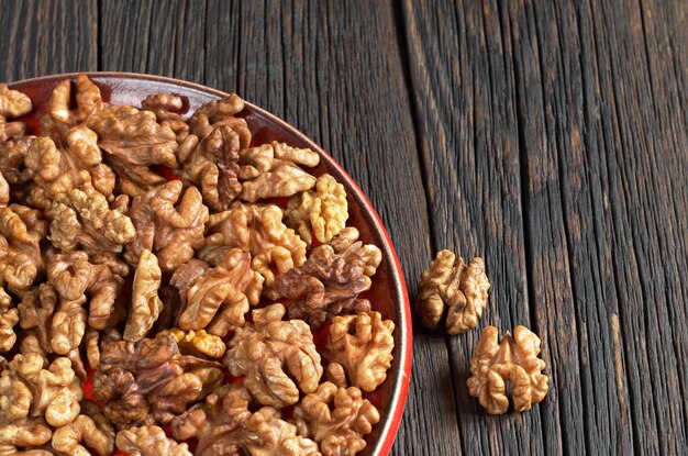 Walnut kernels in red plate on old wooden table with space for text Healthy eating