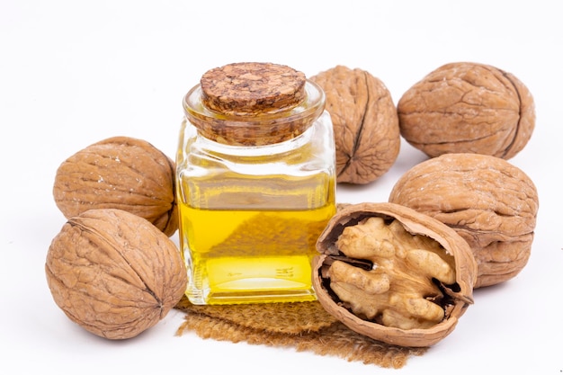 Walnut oil in a glass transparent bottle, walnuts close up isolated on white background