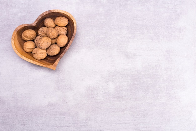 Walnut on a plate in the shape of a heart on gray table background