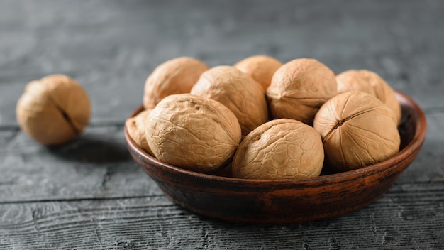 Walnuts in a clay bowl on a dark wooden table.