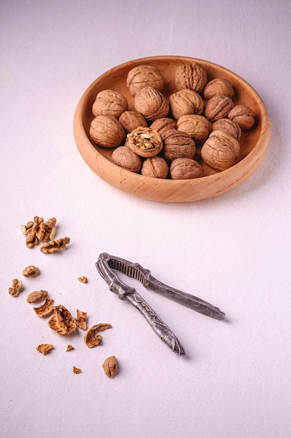 Walnuts heap food in wooden bowl with half peeled nut, cracked nutshell, near to vintage nutcracker on white background, angle view, healthy food concept