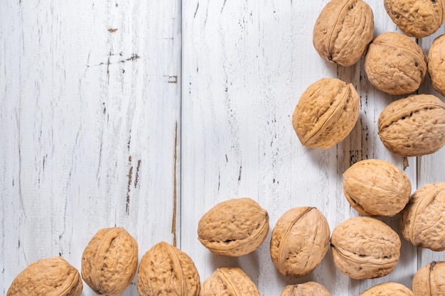 Walnuts kernels on white wooden desk with place for text. Top view of pile of whole walnut shells