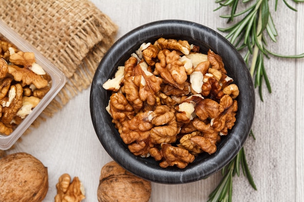 Walnuts in stone bowl and plastic container on a wooden background.