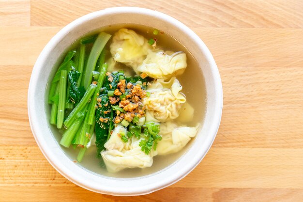 Wanton soup with morning glory and deep fried garlic in bio paper bowl on wooden background.