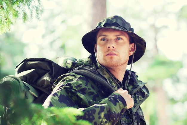 war, hiking, army and people concept - young soldier or ranger with backpack in forest