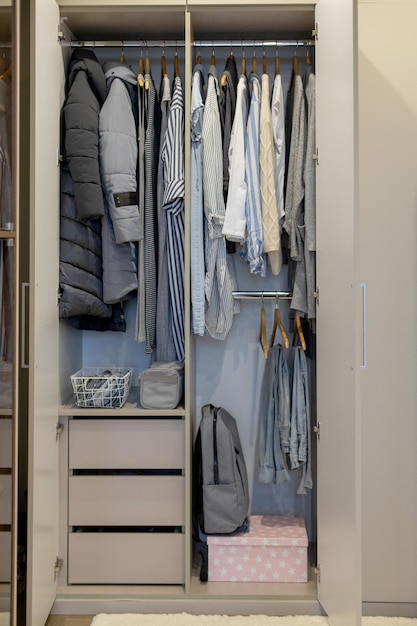 Wardrobe with perfect order clothes in blue and light shades on the hangers and things in containers