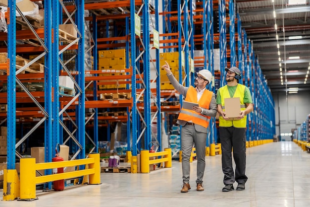 A warehouse man is holding shipment and walking around facility with his supervisor