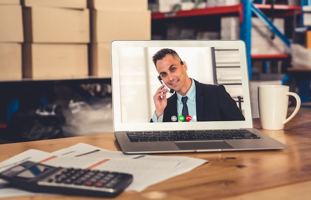 Warehouse staff talking on video call at computer screen in storage warehouse